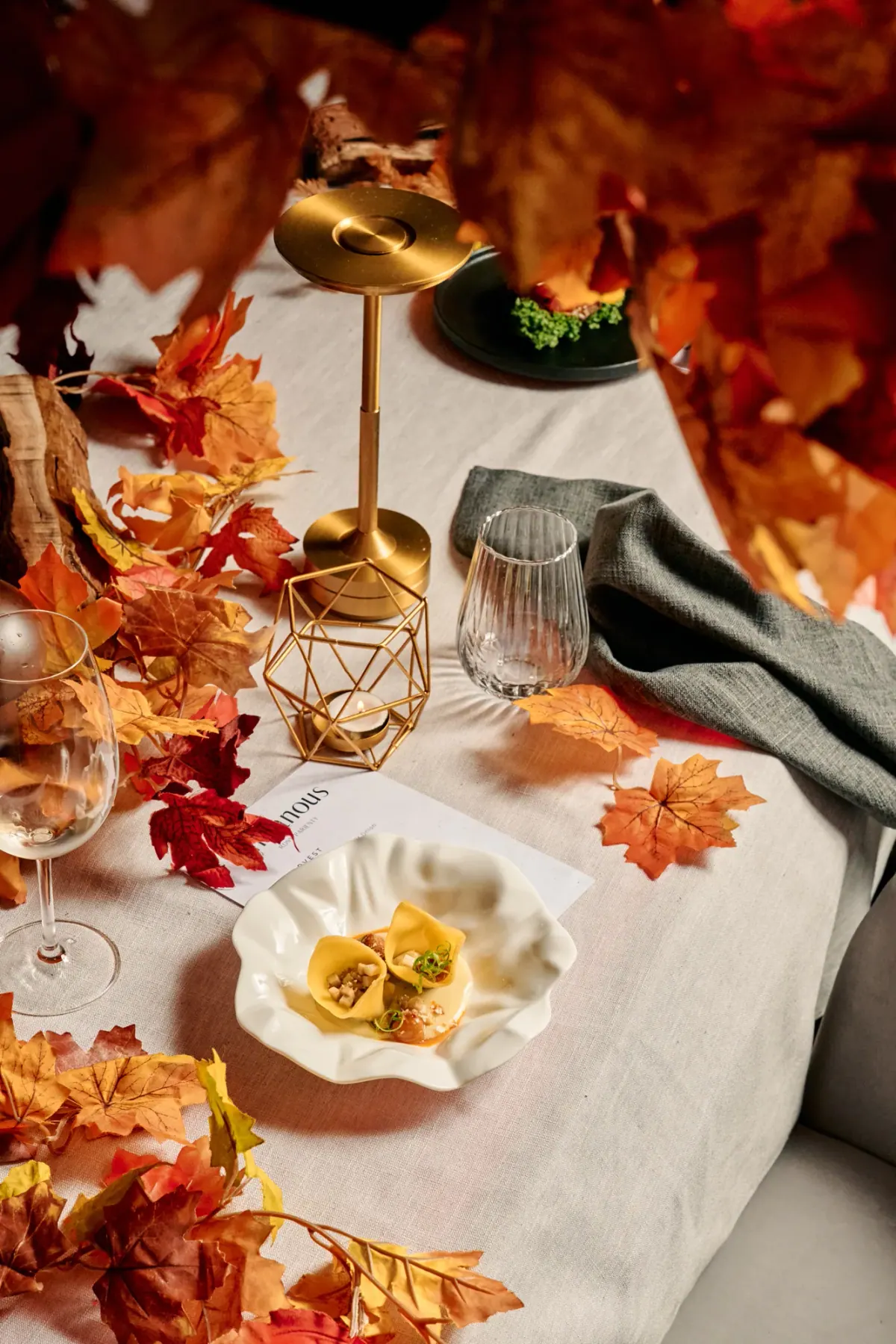 An autumn place setting with maple leaves, a gold lamp and the menu card