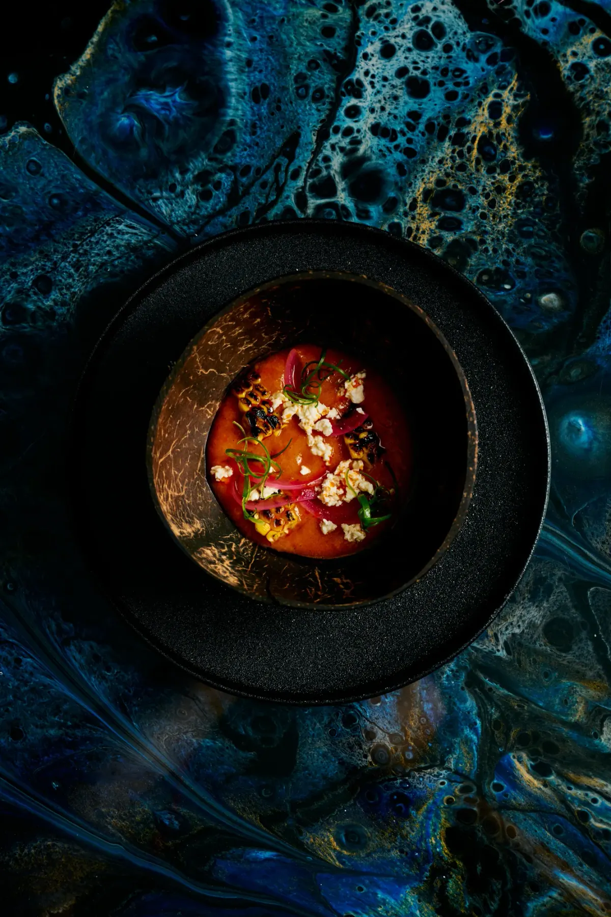 A red broth with crisp toppings in a dark bowl