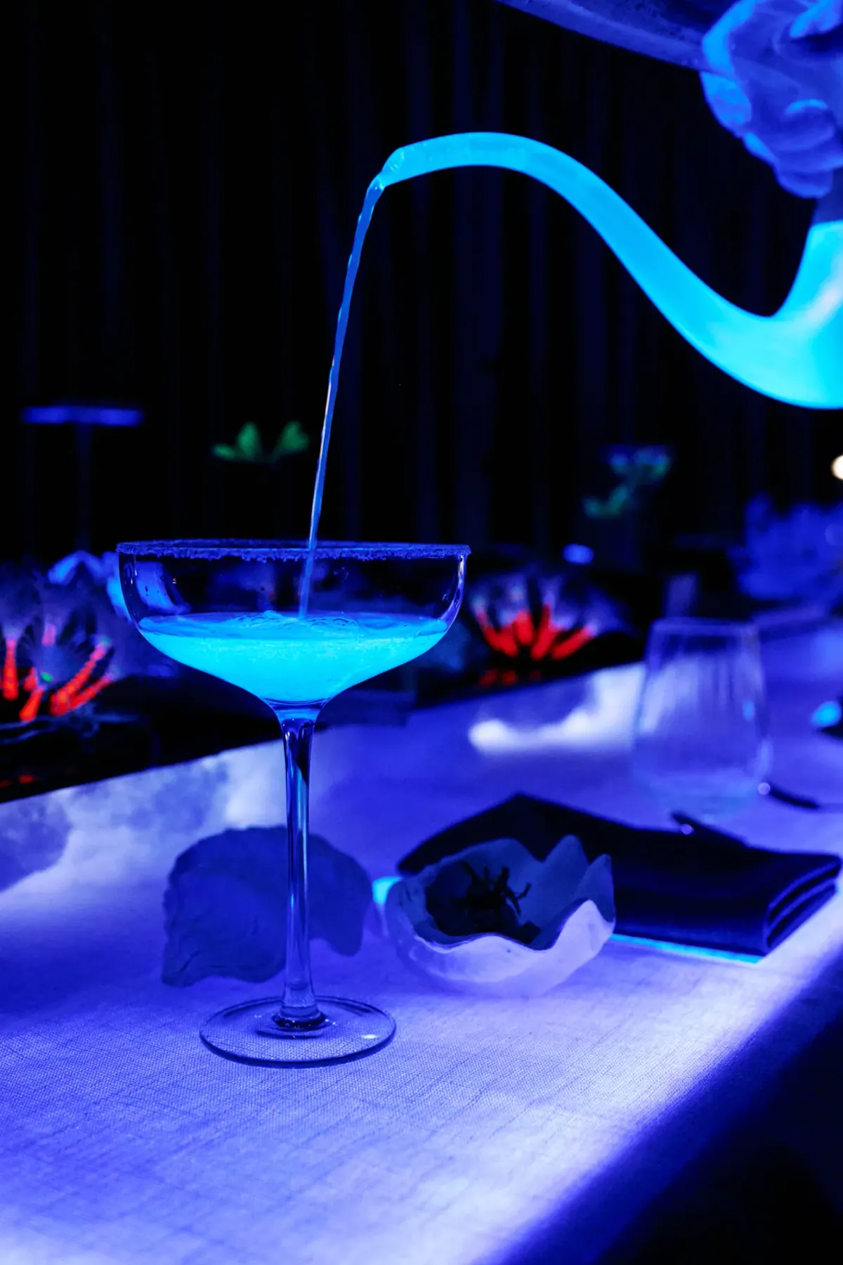 A glowing blue cocktail poured at the table in the dark