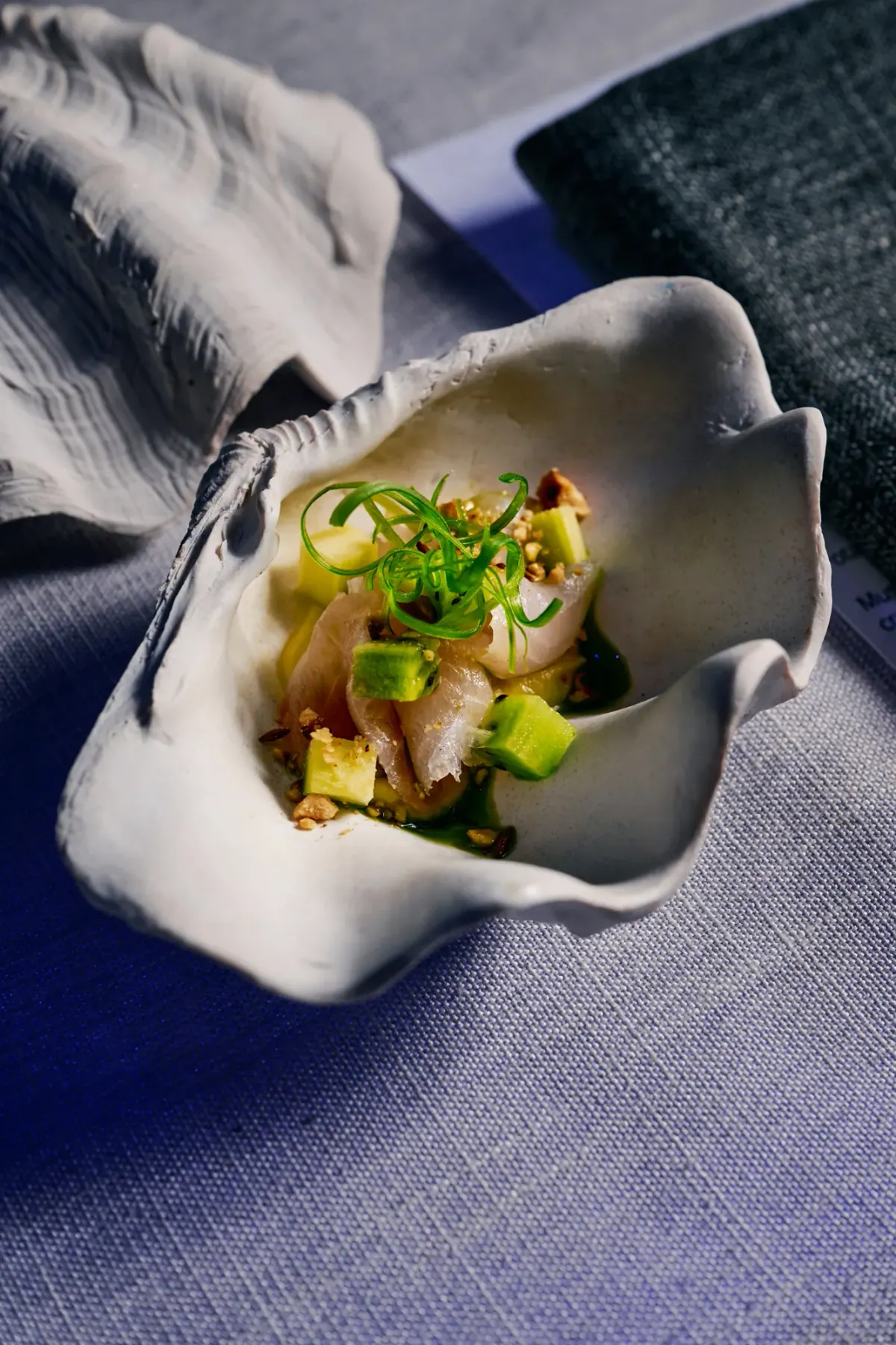 Raw fish with spring onion and cucumber in a white shell dish