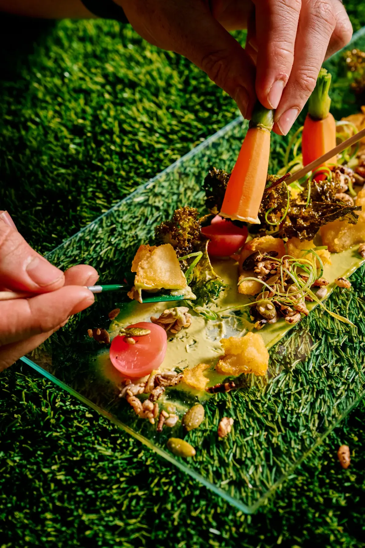 Tweezers finishing a garden course of roasted vegetables on a glass board
