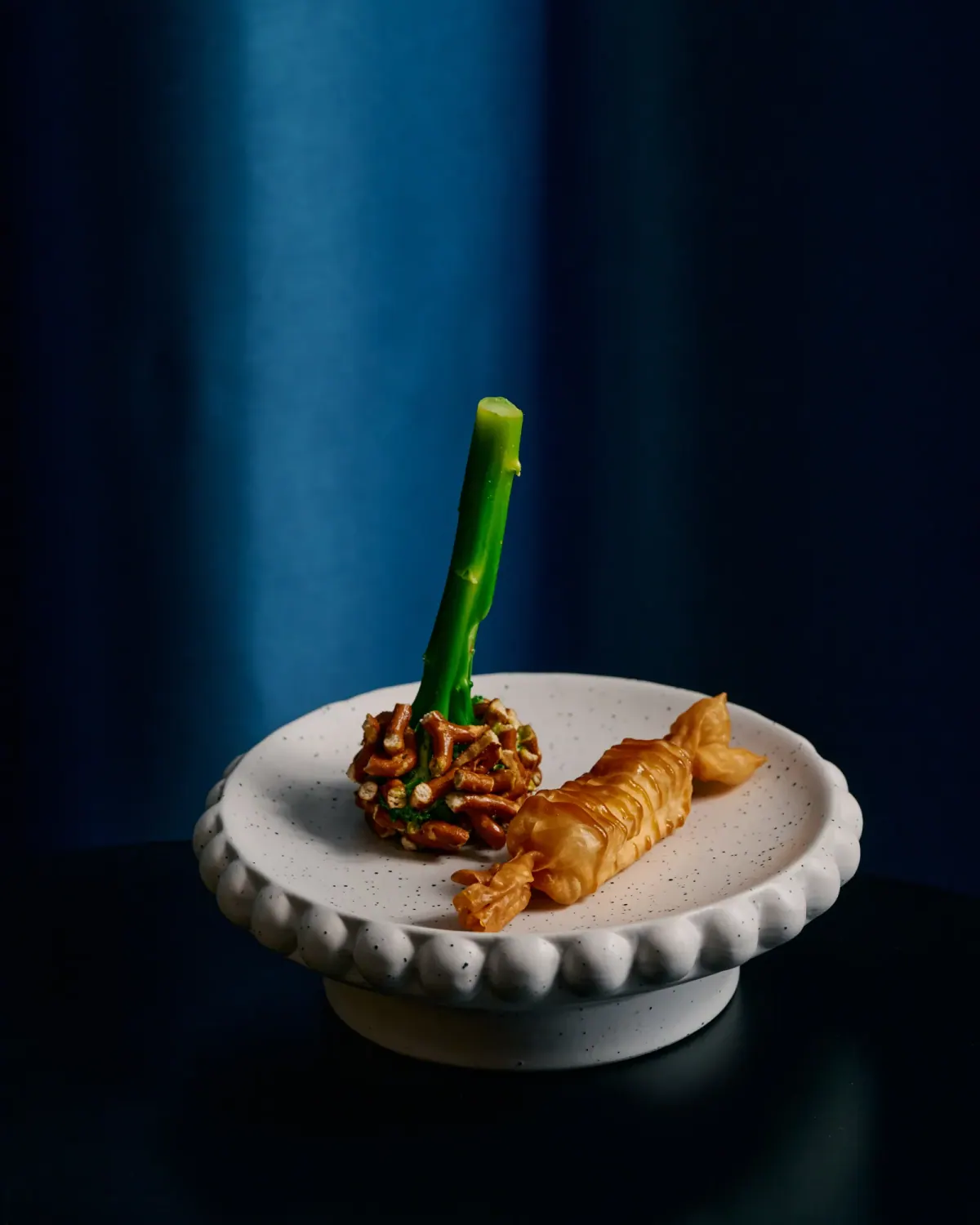 A prawn course with a green stalk on a scalloped white plate